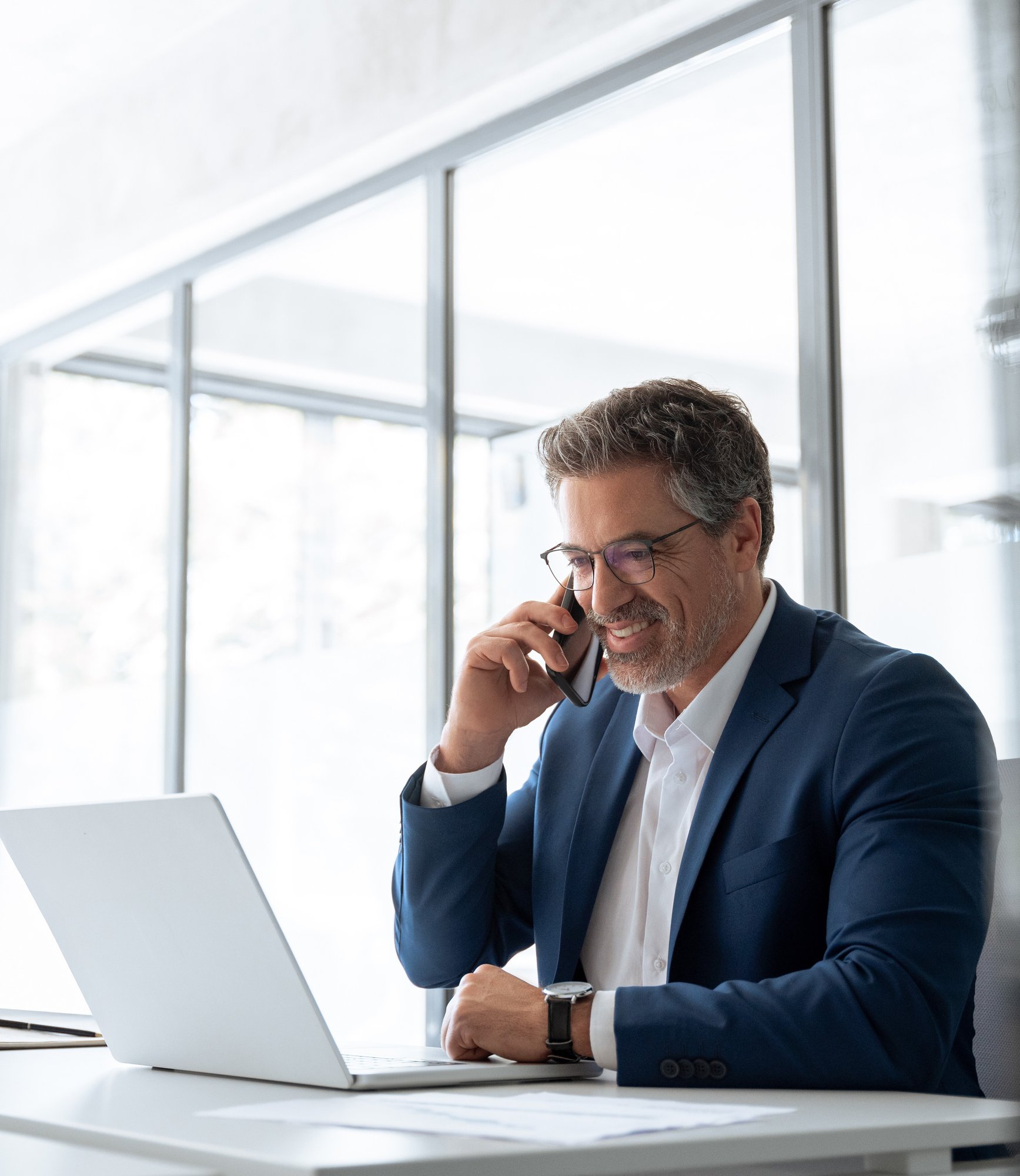 business man talking on the phone and looking at laptop in bright office