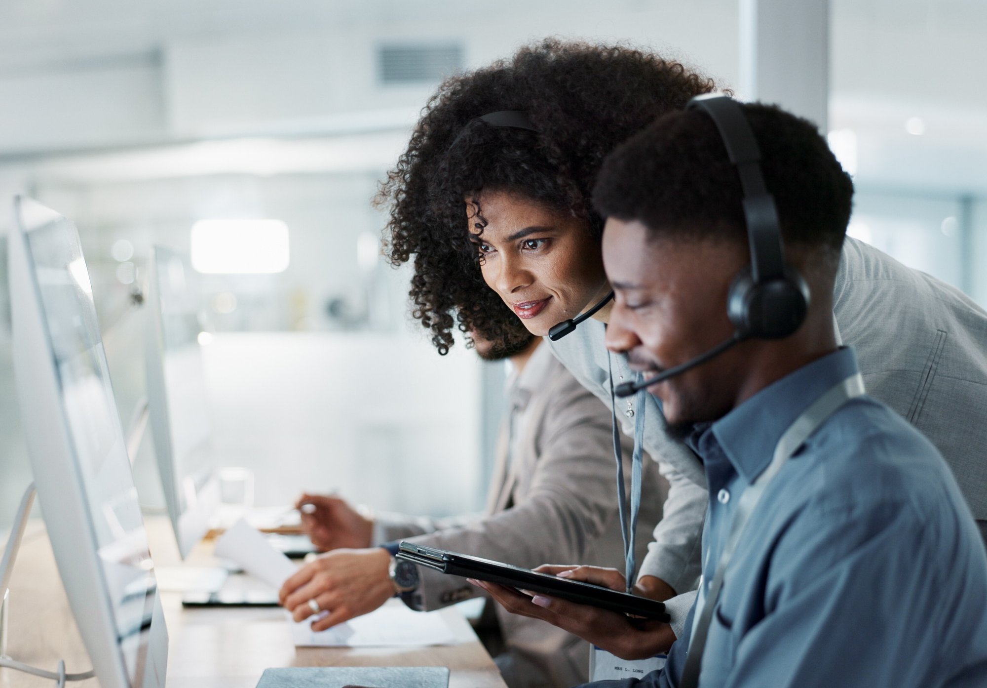 man and woman with headsets looking at computer in brightly lit office