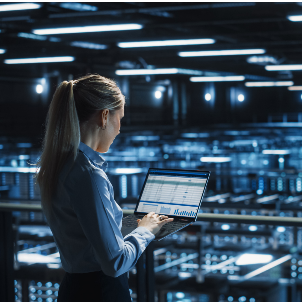 Woman in server room looking at analytics on laptop