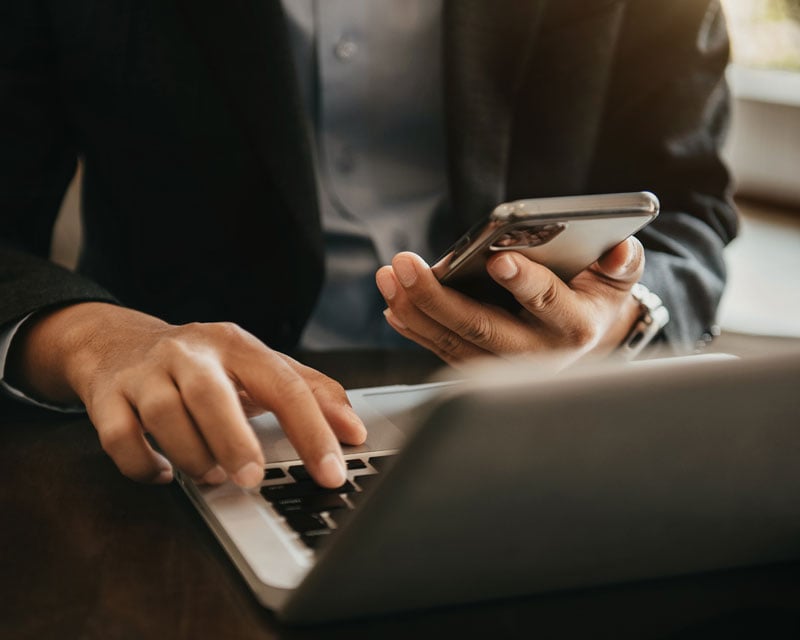 Une personne travaillant sur un ordinateur portable et un appareil mobile.