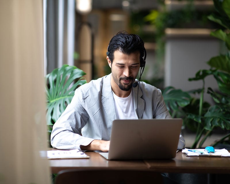 A professional working on laptop while wearing headphones with a microphone.